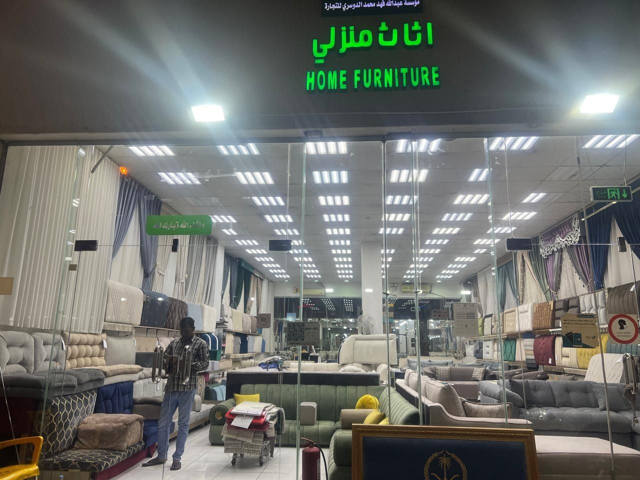 Storefront of a home furniture shop displaying various sofas and cushions inside, with a person browsing.